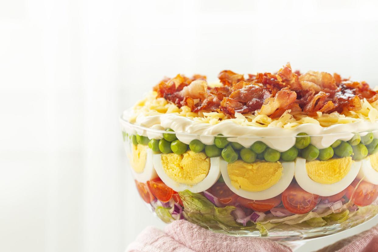 Seven-layer salad. American dish that includes ingredients: iceberg lettuce, tomatoes, red onions, sweet peas, hard boiled eggs, cheddar cheese, and bacon pieces topped with a mayonnaise dressing.