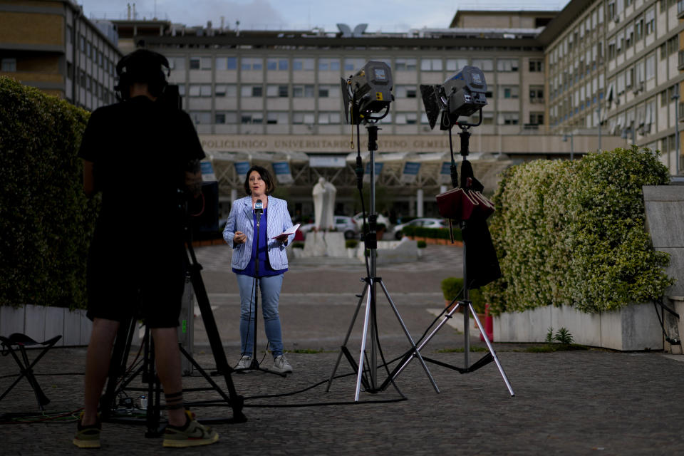 A video journalist talks to camera in front of the Agostino Gemelli University Polyclinic in Rome, Friday, June 9, 2023, where Francis is recovering after undergoing abdominal surgery on Wednesday. The Vatican says Pope Francis has had a second good night in the hospital recovering from surgery to remove intestinal scar tissue and repair a hernia in his abdominal wall. (AP Photo/Andrew Medichini)