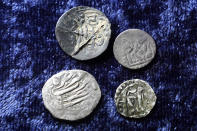 Four 17th century silver coins with Arabic inscriptions rest together on a table in Warwick, R.I., Thursday, Oct. 27, 2022. The coin, at top left, was found in Connecticut, while the other three were found in Rhode Island. One coin at a time, the ground is yielding new evidence that in the late 1600s, every one of the world's most ruthless pirates wandered the American colonies with impunity. (AP Photo/Steven Senne)