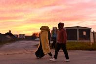 Migrants walk at sunset near the "Jungle" migrant camp in Calais, northern France, on October 27, 2016