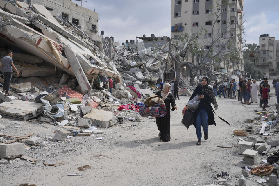 Palestinian women walk by buildings destroyed in Israeli airstrikes in Nuseirat camp in the central Gaza Strip, Monday, Oct. 16, 2023. (AP Photo/Hatem Moussa)