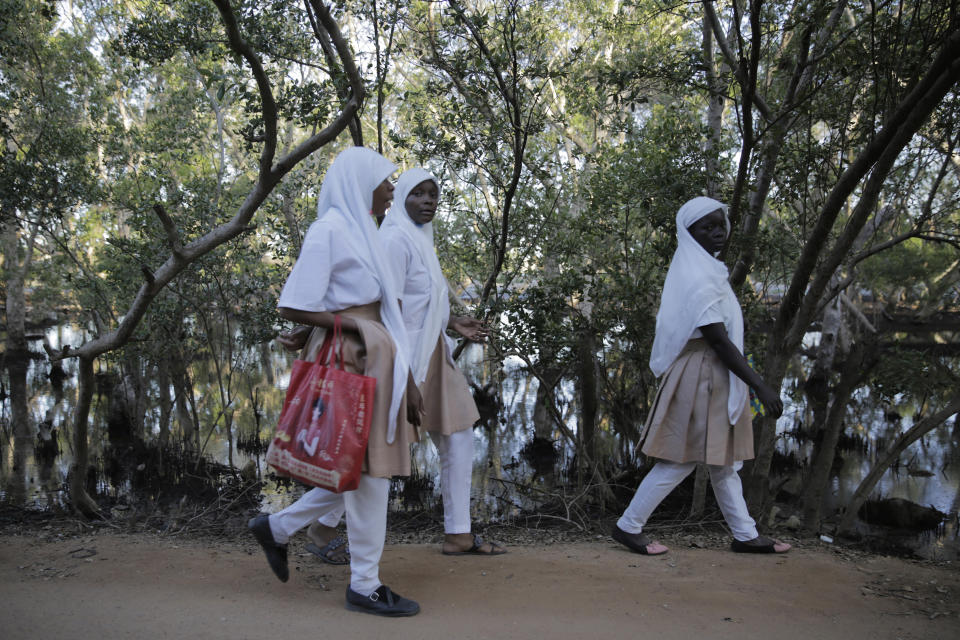 School kids walk past mangrove trees at Vanga, Kwale County, Kenya on Monday, June 13, 2022. Several mangrove forests across Africa have been destroyed due to coastal development, logging or fish farming, making coastal communities more vulnerable to flooding and rising sea levels. (AP Photo/Brian Inganga)