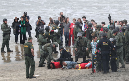 A police officer and a U.S. Customs and Border Protection (CBP) official detain people during a gathering in support of the migrant caravan in San Diego, U.S., close to the border wall between the United States and Mexico, as seen from Tijuana, Mexico December 10, 2018. REUTERS/Mohammed Salem