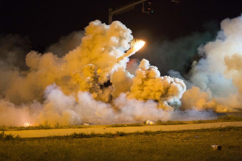 A protester throws back a smoke bomb while clashing with police in Ferguson, Missouri August 13, 2014. Police in Ferguson fired several rounds of tear gas to disperse protesters late on Wednesday, on the fourth night of demonstrations over the fatal shooting last weekend of an unarmed black teenager Michael Brown, 18, by a police officer on Saturday after what police said was a struggle with a gun in a police car. A witness in the case told local media that Brown had raised his arms to police to show that he was unarmed before being killed. Picture taken August 13, 2014. REUTERS/Mario Anzuoni (UNITED STATES - Tags: CRIME LAW)