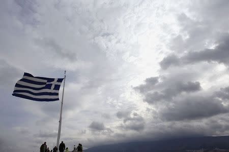 Tourists stand under a Greek national flag atop Acropolis hill in Athens February 22 2015. REUTERS/Kostas Tsironis