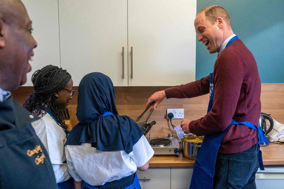 Prince William, Prince of Wales (R) takes part in a cooking lesson with Daisha Nagawagi 12, Inaaya Shahab 13 and and Chef Kevin Muhammad (L) during his visit to Together as One