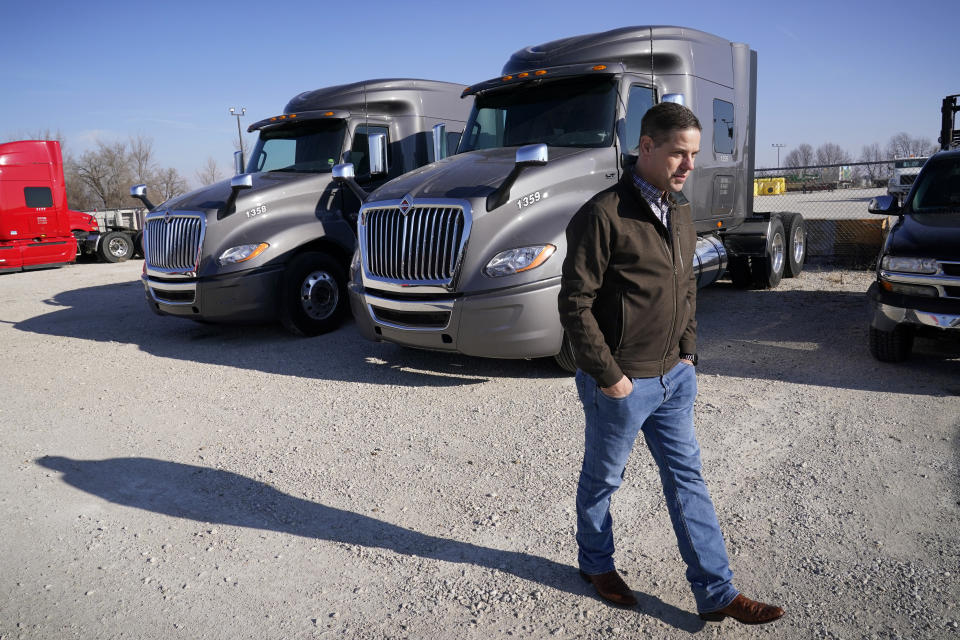 Aaron Tennant walks past vehicles in the lot of his trucking and shipping company, Monday, Dec. 20, 2021, in Colona, Ill. Tennant owns trucking and shipping companies on both the Iowa and Illinois sides of the Mississippi River. This month, after six years under construction, a new bridge opened connecting the town of Bettendorf, Iowa and Moline, Illinois on Interstate 74. But last summer's delays cost Tennant productivity. It frustrated commuters and added extra stress to older bridges. (AP Photo/Charlie Neibergall)
