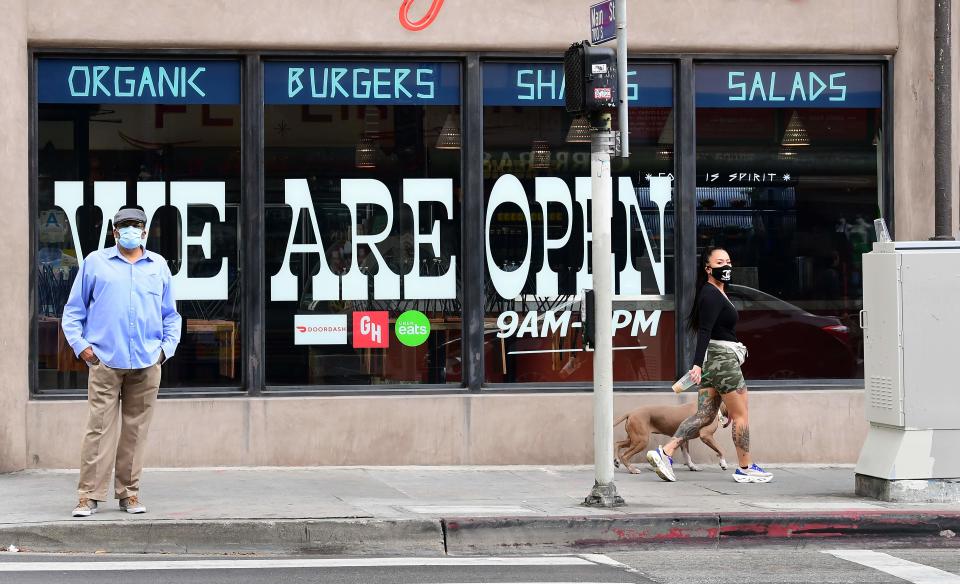 Pedestrians wear facemasks in front of a restaurant in Los Angeles, California on May 12, 2020, as Governor Gavin Newsom announced guidelines for reopening of restaurants, with self-distancing and cleanliness procedures as the state's coronavirus pandemic.