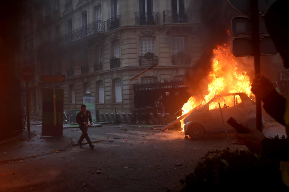 FILE - In this Saturday, Dec.1, 2018 file photo a demonstrator runs pas a burning car during a demonstration in Paris. Protesters angry about rising taxes clashed with French police for a third straight weekend and over 100 were arrested after pockets of demonstrators built barricades in the middle of streets in central Paris, lit fires and threw rocks at officers Saturday. (AP Photo/Thibault Camus, File)