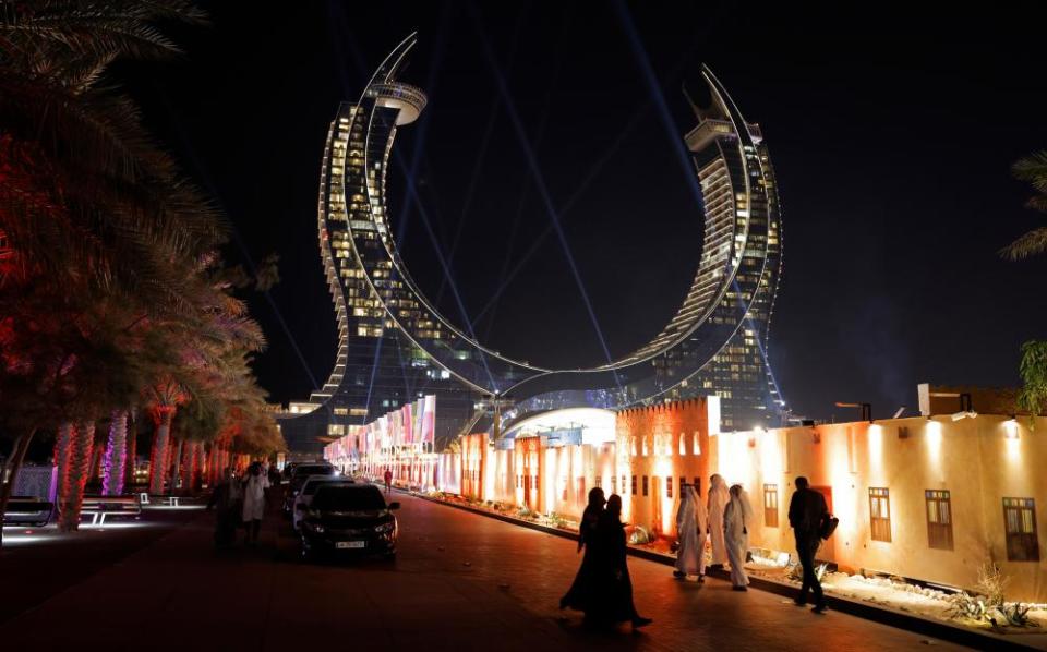 Locals walk past a painted facade made to look like old houses, erected to hide building works going on behind, with in the background the Katara Towers on the seafront in Lusail which houses two luxury hotels, where many FIFA officials are staying.