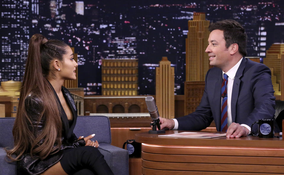 Ariana Grande, in a stylish outfit with long hair in a high ponytail, is interviewed by Jimmy Fallon on "The Tonight Show" set