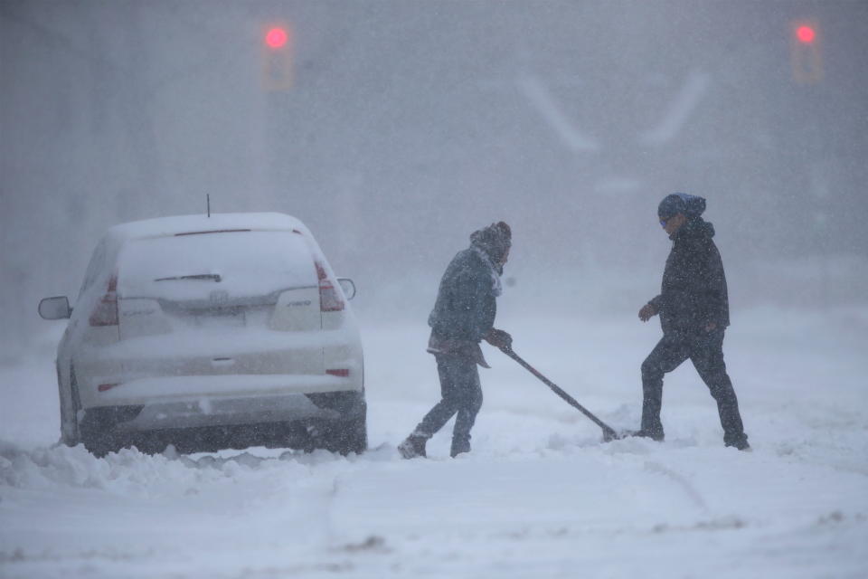 One person shovels snow away from a vehicle while another crosses an empty street as a snowstorm arrives in Winnipeg, Manitoba, Canada April 13, 2022. REUTERS/Shannon VanRaes