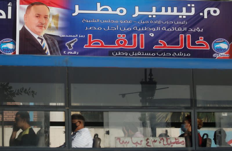Egyptians look out of a bus window in front an election campaign banner of the member of Mostaqbal Watn (Nation's Future) Khaled El Kout before the first round of the parliamentary election in Cairo
