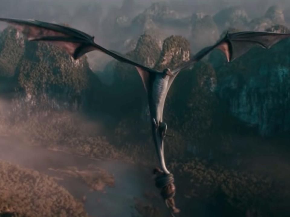 a wyvern takes flight in a mountainous scenery — it's a dragon like creature with wide wings, carrying wizard newt scamander in its tail in fantastic beasts the secrets of dumbledore