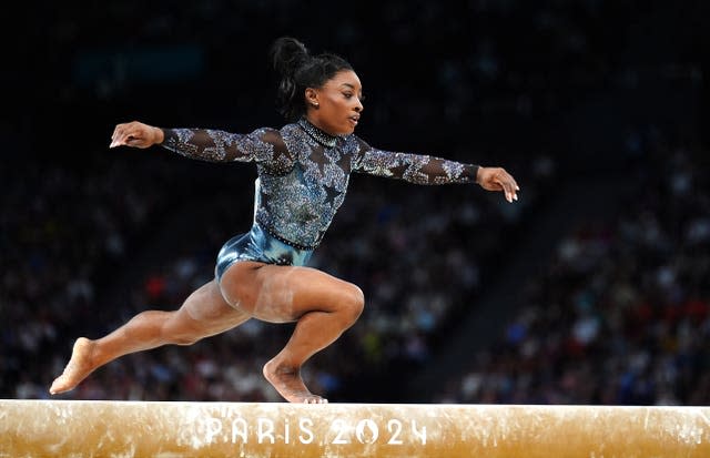 Gymnast Simone Biles performs on the beam, arms outstretched, at the Paris Olympics. 