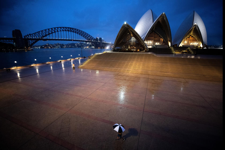 Empty Sydney Opera House forecourt. Lone pedestrian with black and white umbrella. 