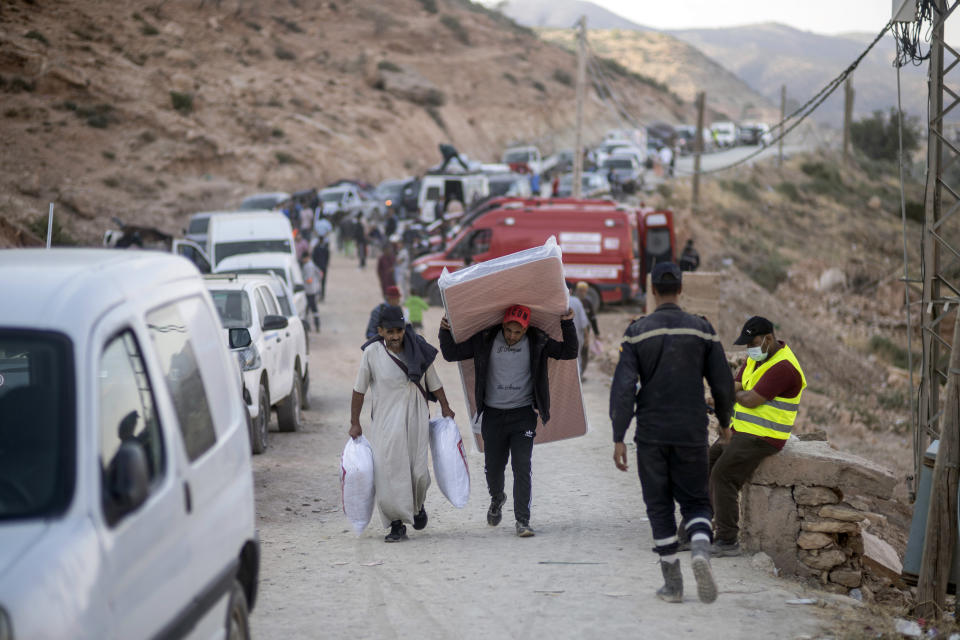 People who were displaced by the earthquake carry humanitarian aid to their tents, in the town of Imi N'tala, outside Marrakech, Morocco, Wednesday, Sept. 13, 2023. An aftershock rattled central Morocco on Wednesday, striking fear into rescue crews at work in High Atlas villages, digging people out from rubble that could slide. (AP Photo/Mosa'ab Elshamy)