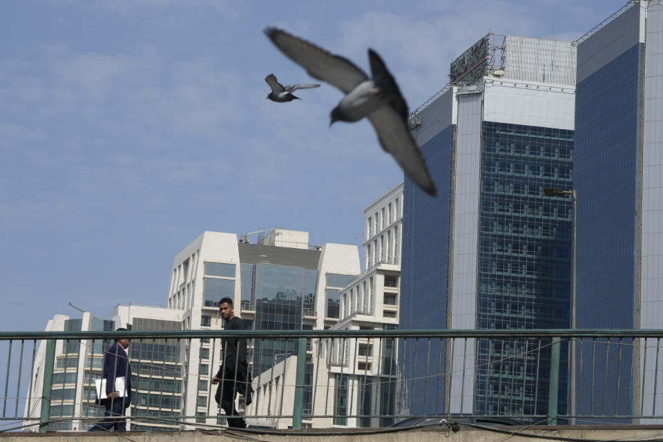 People walk on a bridge in front of the National Bank of Egypt headquarters in Cairo, Egypt, Thursday, Feb. 9, 2023. Egypt is embarking on a privatization push to help its cash-strapped government, after pressure from the International Monetary Fund. The new policy is supposed to be a serious departure for the Egyptian state, which has long maintained a tight grip over sectors of the economy. (AP Photo/Amr Nabil)