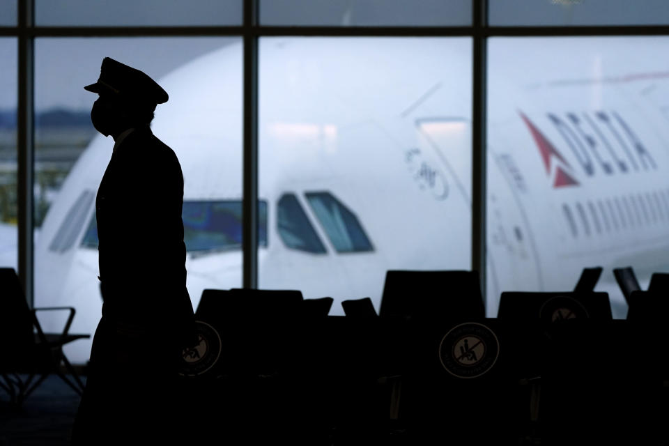 FILE - A Delta Airlines pilot wears a face mask as he walks through a terminal at Hartsfield-Jackson International Airport in Atlanta, on Thursday, Feb. 18, 2021. Airlines executives told legislators on Wednesday, Dec. 15 they are having trouble hiring pilots, flight attendants and other personnel, and that’s part of what is causing canceled flights and scrapping of service to some airports. (AP Photo/Charlie Riedel, File)