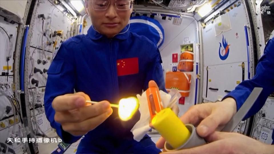 two astronauts in blue spacesuits hold a match and a candle, respectively