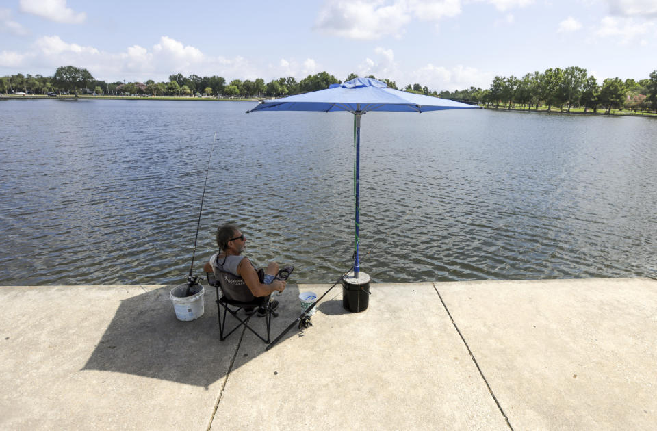 Lee Guidry fishes for catfish from under an umbrella at Lafreniere Park in Metairie, La., on Tuesday, June 27, 2023. (Brett Duke/The Advocate via AP)