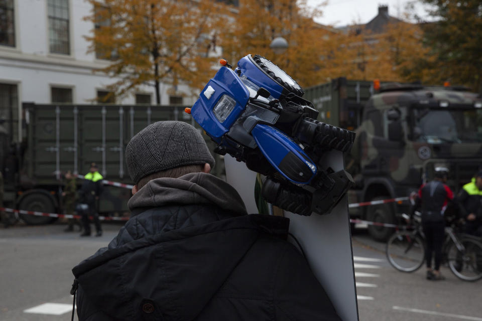 A lone protestor holds a sign on a crossing where Dutch army trucks block the road to prevent protesting farmers from reaching parliament in The Hague, Netherlands, Wednesday, Oct. 16, 2019. Thousands of Dutch farmers protest over the Netherlands efforts to drastically reduce emissions of greenhouse gases. Among the farmers' demands are that the government does not further reduce the number of animals they can keep. (AP Photo/Peter Dejong)