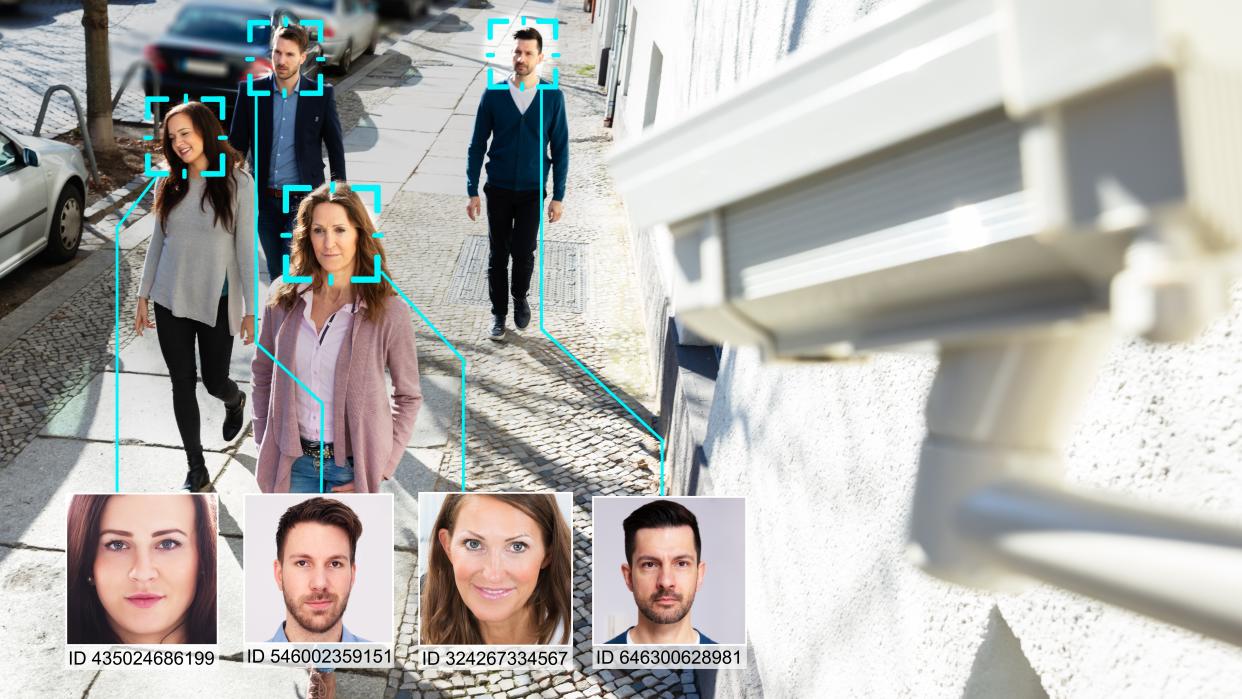  Stock photo of four people on the street being monitored by a facial recognition camera. 