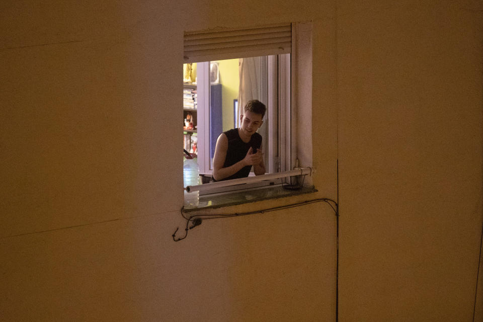 FILE - In this March 15, 2020, file photo, a man applauds from his window in support of the medical staff in Madrid, Spain. At a time of unfathomable isolation, people in many European cities hit hard by the new coronavirus are taking at least a minute to come together in gratitude as they stand at open windows or on balconies singing, cheering and applauding. (AP Photo/Paul White, File)