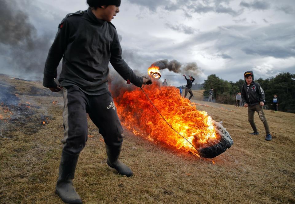 In this photo taken on Sunday, March 10, 2019, children spin burning tires during a ritual marking the upcoming Clean Monday, the beginning of the Great Lent, 40 days ahead of Orthodox Easter, on the hills surrounding the village of Poplaca, in central Romania's Transylvania region. Romanian villagers burn piles of used tires then spin them in the Transylvanian hills in a ritual they believe will ward off evil spirits as they begin a period of 40 days of abstention, when Orthodox Christians cut out meat, fish, eggs, and dairy. (AP Photo/Vadim Ghirda)