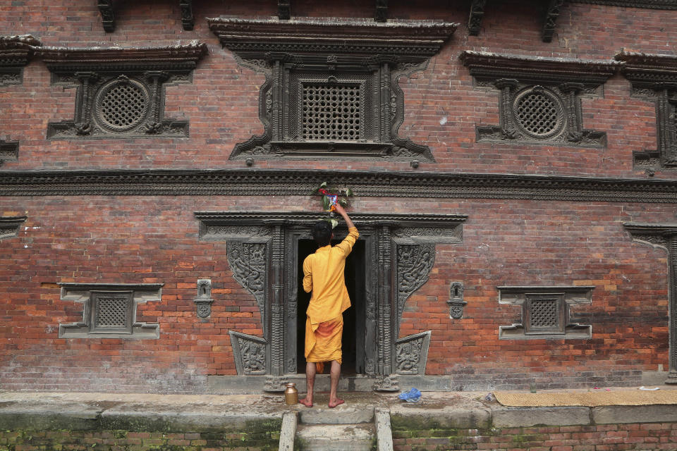 In this Aug. 5, 2019, photo, a Nepalese priest displays a machine made painting above the door of a temple during Naag Panchami festival in Bhaktapur, Nepal. The art and tradition of Nepal’s Chitrakar families, who depicted gods and goddesses on temples, masks of Hindu deities and posters for various religious celebrations is dying because of mass machine printed posters and card-size pictures of gods that are cheaper and more popular. (AP Photo/Niranjan Shrestha)