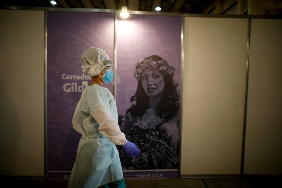 A social worker walks past a poster of Argentine singer Gilda at Tecnopolis Park which has been repurposed as a shelter to quarantine COVID-19 patients who are asymptomatic or have light symptoms, in Buenos Aires, Argentina, Tuesday, Sept. 1, 2020.