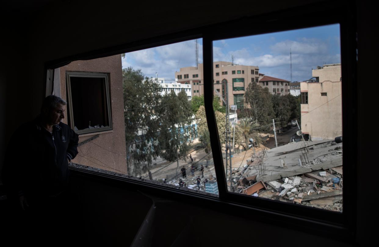 A Palestinian man looks from a broken window at the remains of a six-story building destroyed by an early morning Israeli airstrike in Gaza City on Tuesday, May 18, 2021. Israel carried out a wave of airstrikes on what it said were militant targets in Gaza, leveling a six-story building in downtown Gaza City, and Palestinian militants fired dozens of rockets into Israel early Tuesday, the latest in the fourth war between the two sides, now in its second week.