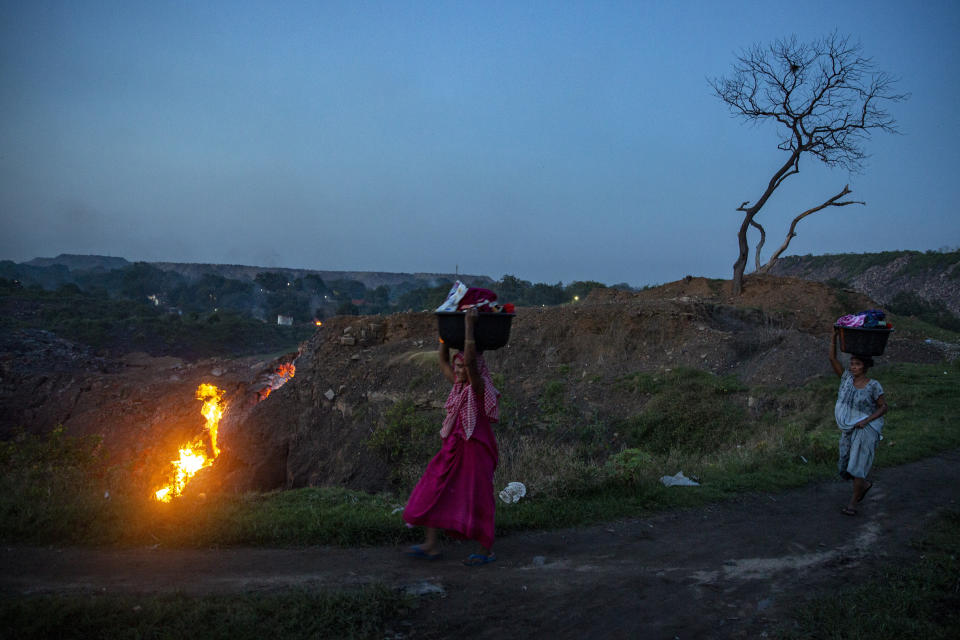 FILE- Women walk past as flames rise out of fissures in the ground above coal mines in the village of Liloripathra near Dhanbad, an eastern Indian city in Jharkhand state, Friday, Sept. 24, 2021. India has yet to submit its targets for cutting greenhouse emissions to the U.N climate agency. Four months have passed since Indian Prime Minister Narendra Modi announced its 'net-zero' target and short-term goals for increasing clean energy. (AP Photo/Altaf Qadri,file)