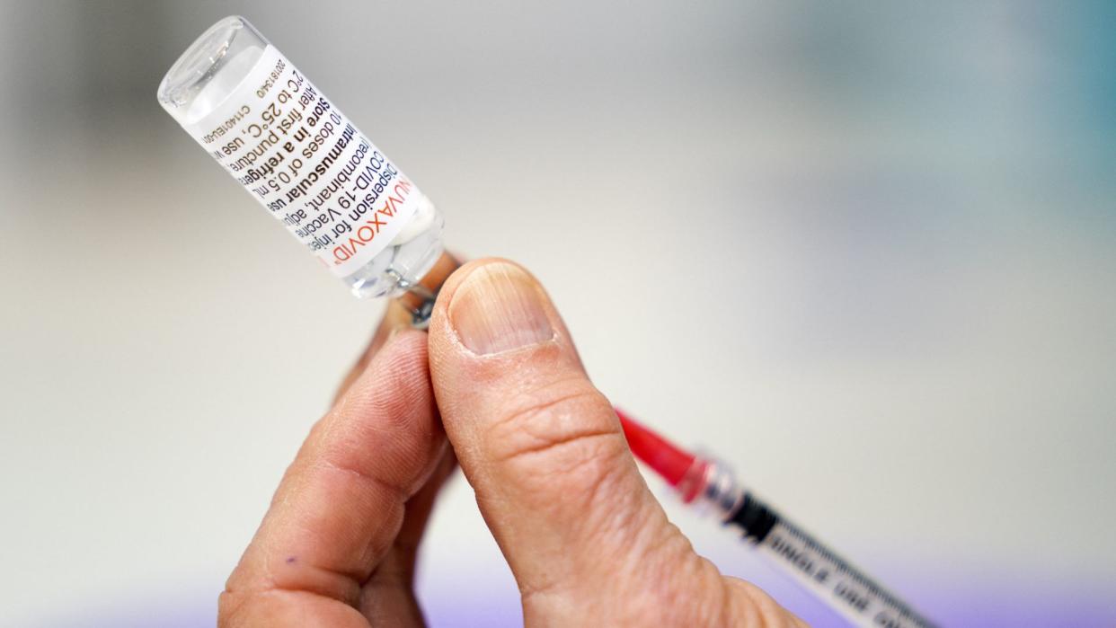  Close up of a person's hand as they extract vaccine from a vial labeled "novavax". 