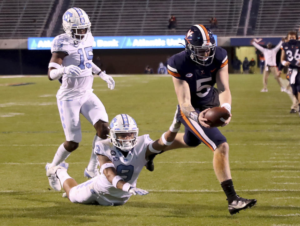 FILE - Virginia quarterback Brennan Armstrong (5) reaches for a touchdown next to North Carolina defensive back Cam'Ron Kelly (9) and defensive back DeAndre Hollins (15) during an NCAA college football game in Charlottesville, Va., in this Saturday, Oct. 31, 2020, file photo. Louisville has paused all football activities and its Saturday game at Virginia has been postponed at least a week due to a spike in COVID-19 cases. Louisville athletic director Vince Tyra told reporters Wednesday night, Nov. 4, the program has 10 players who have tested positive for COVID-19 and five players who were in quarantine because of contact tracing. Five support staff members also tested positive and two others are in quarantine.(Andrew Shurtleff/The Daily Progress via AP, File)