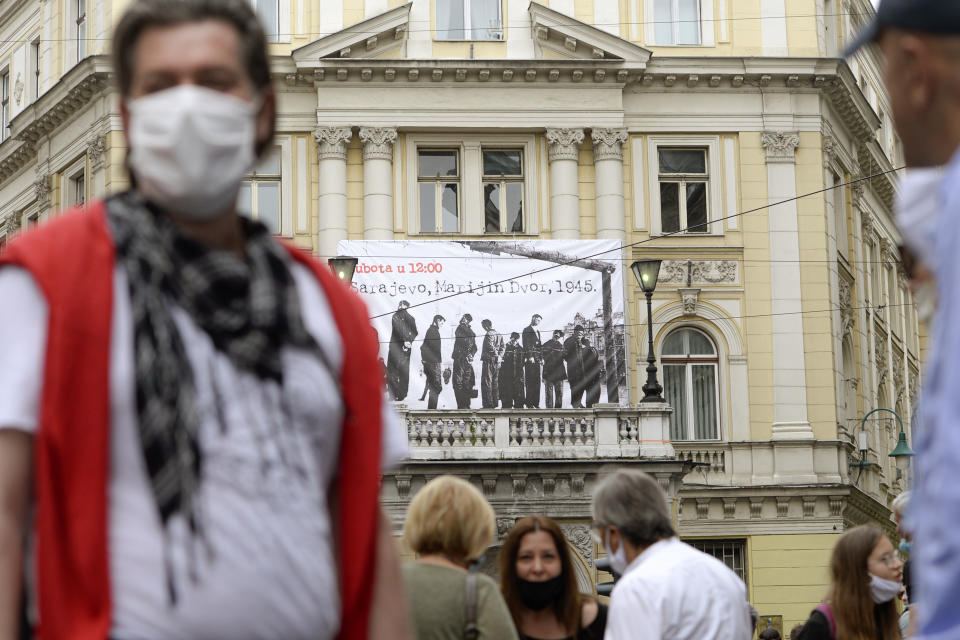 People walk backdropped by a banner showing victims executed by hanging in 1945 by the pro-Nazi Croatian WWII Ustasha regime, responsible for sending tens of thousands of Serbs, Gypsies and Jews to their death in concentration camps, during a commemoration at the Sacred Heart Cathedral in Sarajevo, Bosnia, Saturday, May 16, 2020. Bosnian Catholic clerics along with Croatian state representatives and members of the Bosnian Croats community attended a religious service commemorating the massacre of Croatian pro-Nazis by victorious communists at the end of World War II. (AP Photo/Kemal Softic)