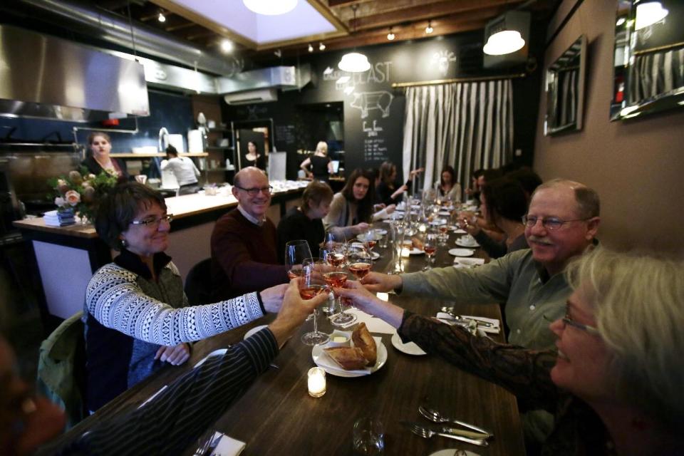 This Sept. 27, 2013 photo shows patrons toasting at Naomi Pomeroy's Beast restaurant in Portland, Ore., where diners enjoy a six-course prix fixe dinner built around massive flavors and the chef’s penchant for butchering whole animals. The rustic, yet refined menu changes weekly, but you can expect the likes of charcuterie plates with steak tartare and mains of braised pork belly. (AP Photo/Don Ryan)