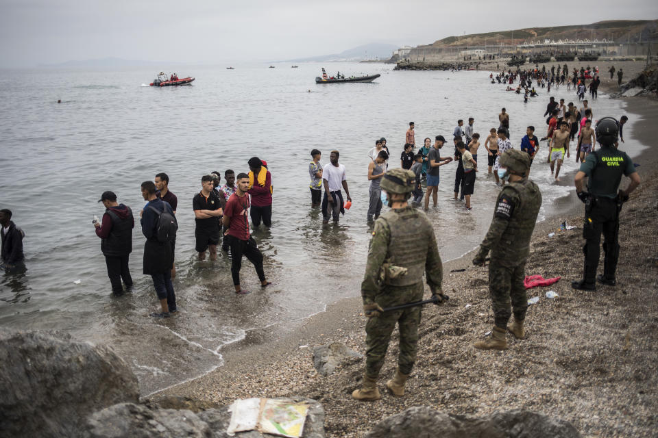 People mainly from Morocco stand on the shore as Spanish Army cordon off the area at the border of Morocco and Spain, at the Spanish enclave of Ceuta, on Tuesday, May 18, 2021. About 8,000 people have streamed into the Spanish city of Ceuta from Morocco in the past two days in an unprecedented influx of migrants, most of them swimming across the border to reach the Spanish enclave in North Africa. (AP Photo/Javier Fergo)