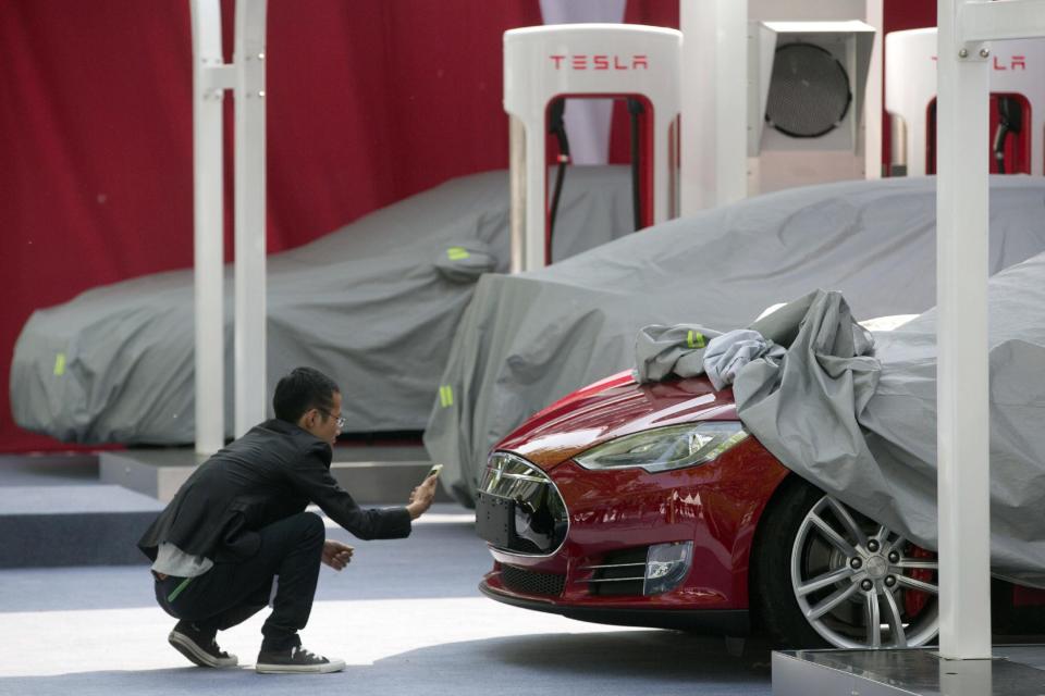A man takes a photo of the logo on a Tesla Model S sedan at an event in Beijing, China, Tuesday, April 22, 2014. Tesla Motors delivered its first eight electric sedans to customers in China on Tuesday and CEO Elon Musk said the company will build a nationwide network of charging stations and service centers as fast as it can. (AP Photo/Ng Han Guan)