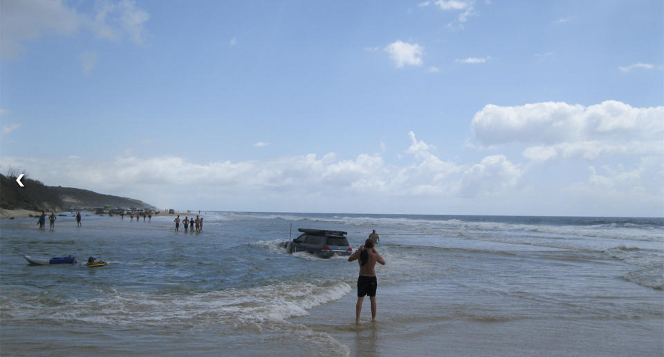 A 4WD travels through sea water on Fraser Island as holiday-makers walk on the sand