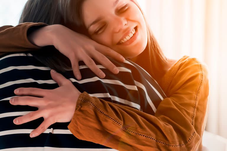 Two friends are embracing in the sun and happy to meet each other. Girls celebrate the holidays or anniversary and hug tightly and warm, feel an emotional connection  and love, smiley face closeup.