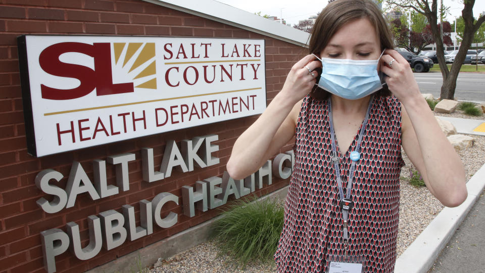 In this Tuesday, May 19, 2020, photo, health investigator Mackenzie Bray adjusts her mask at the Salt Lake County Health Department, in Salt Lake City. Bray normally works to track contacts for people with sexually transmitted diseases, but she was re-assigned during the coronavirus pandemic. She is now one of 130 people at this county health department assigned to track down COVID-19 cases in Utah's urban center around Salt Lake City. The investigators, many of them nurses, each juggle 30 to 40 cases that can include a total of several hundred people. (AP Photo/Rick Bowmer)