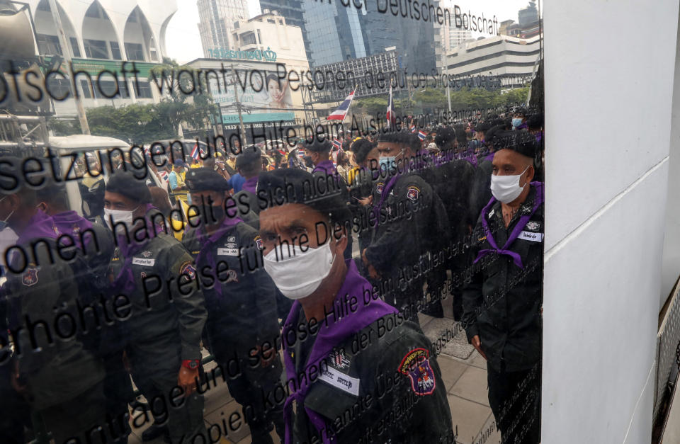 Police officers and supporters of the Thai monarchy are reflected on the sign of the German Embassy in central Bangkok, Thailand Monday, Oct. 26, 2020. The royalists gathered to defend pro-democracy protesters' contention that King Maha Vajiralongkorn spends much of his time in Germany conducting Thai political activities. German government officials have recently expressed concern over political activities the king might be conducting on the Germany's soil. (AP Photo/Gemunu Amarasinghe)