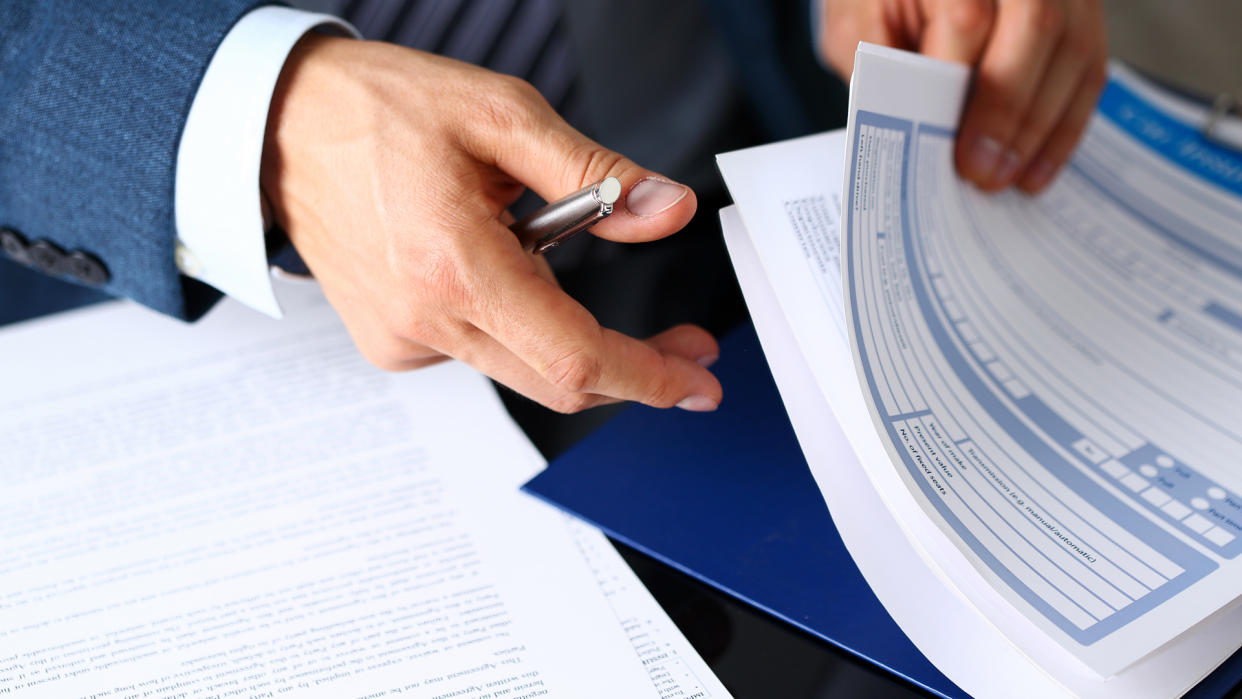 Male arm in suit offer insurance form clipped to pad and silver pen to sign closeup.