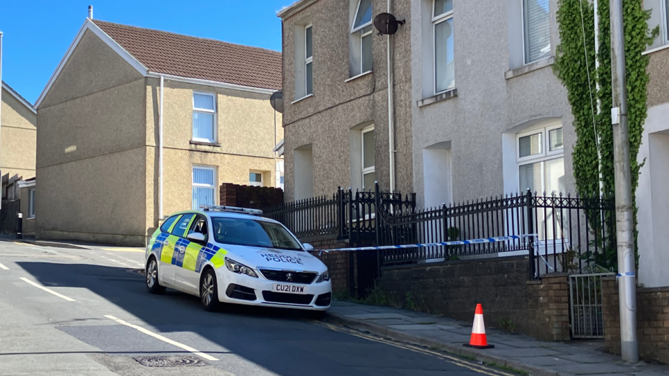 A police car in Bigyn Road, Llanelli, with police tape around the front of a house