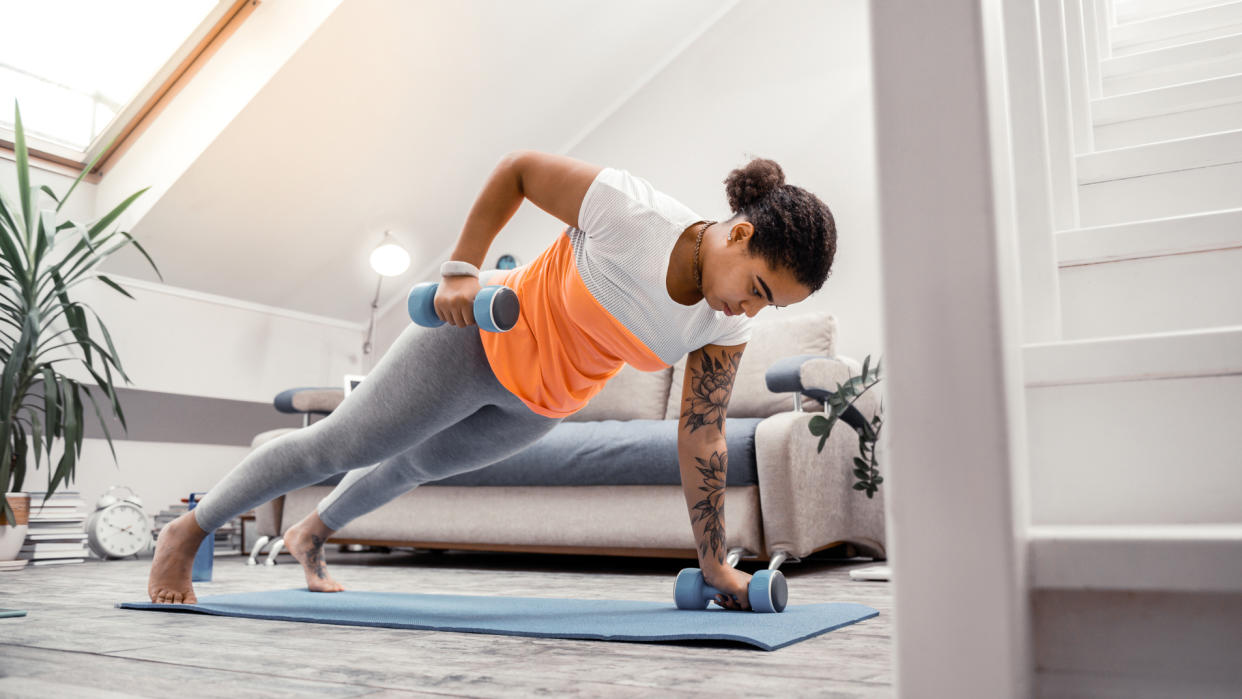  A woman in workout clothing performing a renegade row at home with dumbbells. 