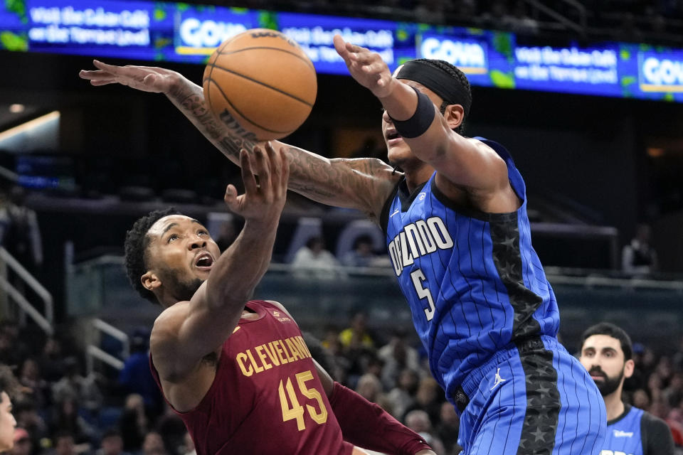 Cleveland Cavaliers guard Donovan Mitchell (45) gets off a shot in front of Orlando Magic forward Paolo Banchero (5) during the first half of an NBA basketball game, Monday, Dec. 11, 2023, in Orlando, Fla. (AP Photo/John Raoux)