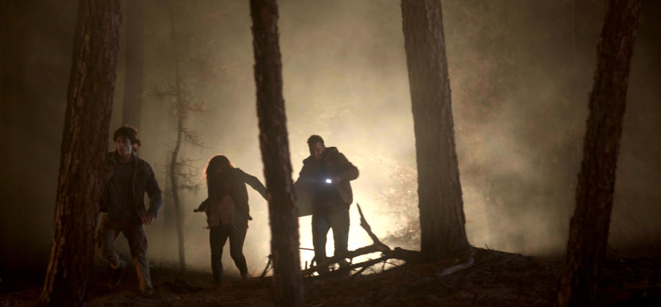 Three people walking through smoke in a forest during a wildfire.