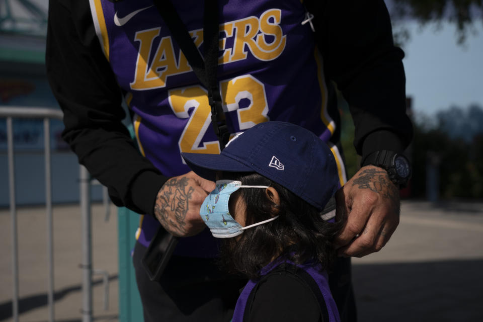 Eric Alcocer puts a mask on his daughter, Amari, 3, while waiting in line to enter Adventure City amusement park on the day of reopening in Anaheim, Calif., Friday, April 16, 2021. The family-run amusement park that had been shut since March last year because of the coronavirus pandemic reopened on April 16. (AP Photo/Jae C. Hong)