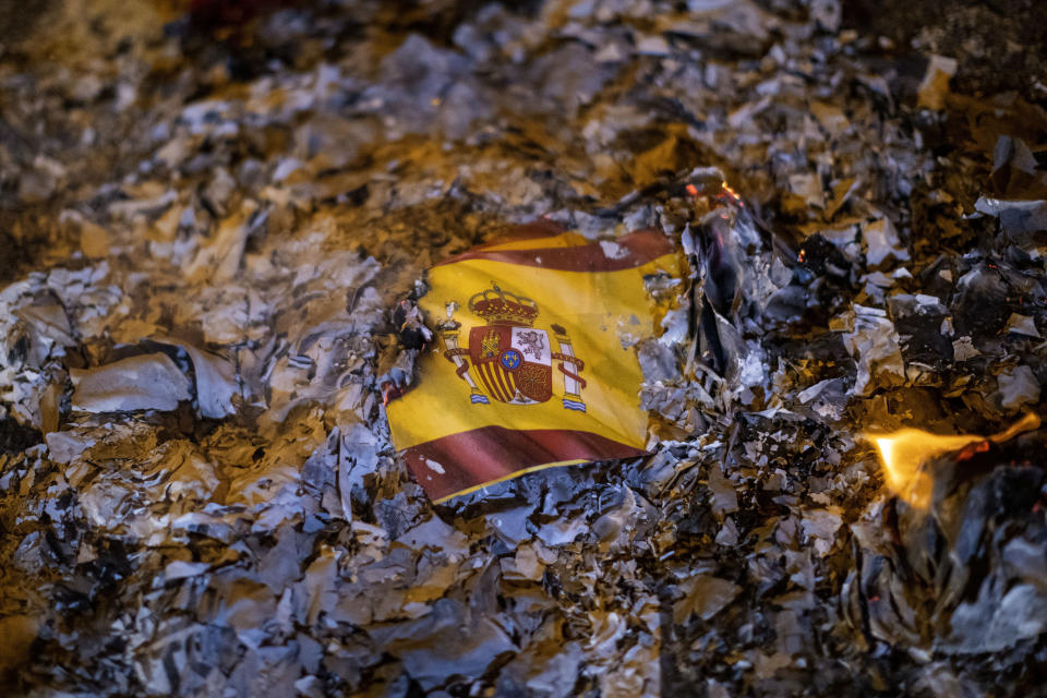 FILE - The remains of a partially burned Spanish flag lie among ashes during a protest against the visit of members of the Spanish Royal Family in Barcelona, Spain, Monday, Nov. 4, 2019. Thousands of ordinary citizens got into legal trouble for their parts in Catalonia’s illegal independence bid that brought Spain to the brink of rupture six years ago. Now they are hoping to be saved. Spain’s acting prime minister, Pedro Sánchez, is negotiating with Catalan separatist parties on the possibility of issuing a sweeping amnesty for the separatists in exchange for their helping him form a new national government in Madrid. (AP Photo/Emilio Morenatti, File)